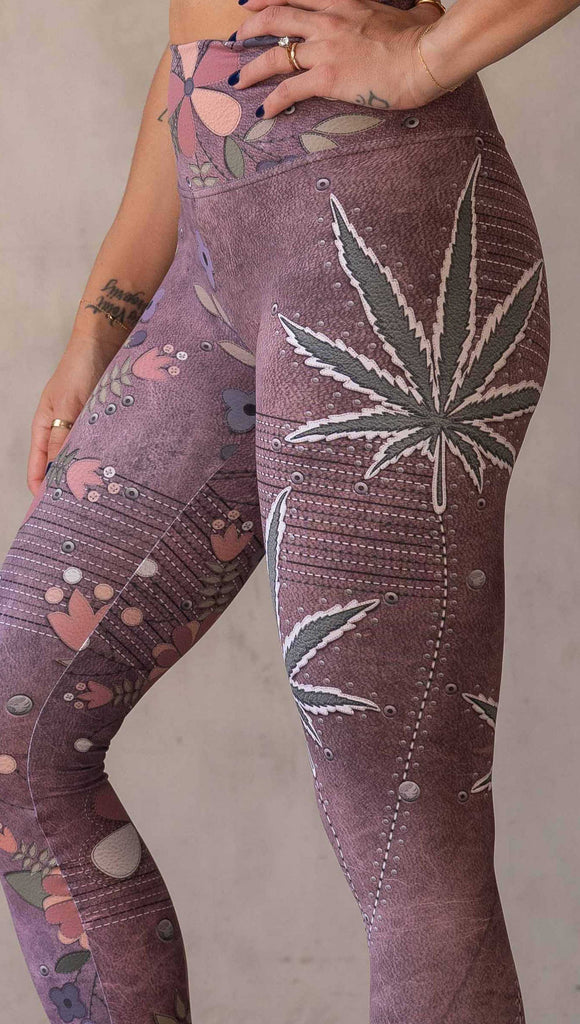 Model wearing WERKSHOP Dope + Flowers Mashup leggings. The leggings are printed with original artwork by Chriztina Marie. One leg features patchwork daisys over grainy mauve toned leather background. The other leg features marijuana leaves over a warm brown background. Both legs have faux stitching.