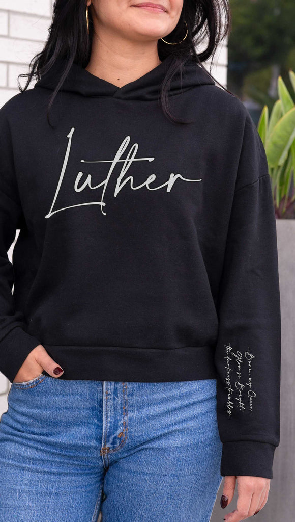 WERKSHOP  "Luther" Boyfriend Hoodie. Officially licensed from Spark of the Everflame by Penn Cole. The hoodie has "Luther" on the front chest
... and "Burn, my Queen. Glow so Bright, the darkness trembles" on the sleeve. Shown here in Black with white writing.