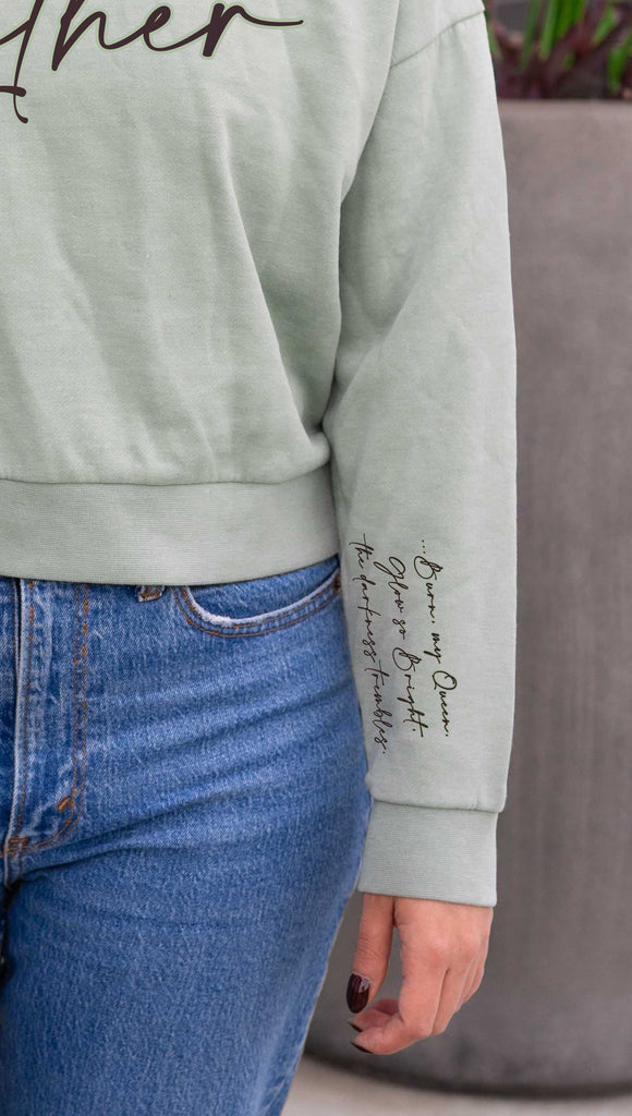 Model wearing WERKSHOP  "Luther" Boyfriend Hoodie. Officially licensed from Spark of the Everflame by Penn Cole. The hoodie has "Luther" on the front chest
... and "Burn, my Queen. Glow so Bright, the darkness trembles" on the sleeve. Shown here in Sage with dark taupe writing.