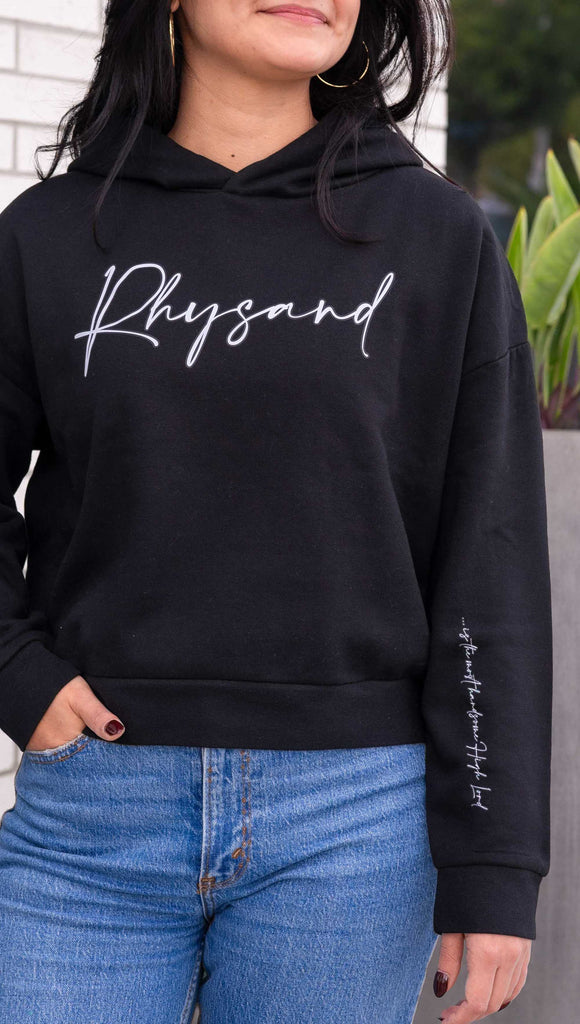 Model wearing WERKSHOP "Rhysand" Hoodie. Officially licensed for Sarah J Maas. The hoodie says, "Rhysand" on the chest and "... is the most handsome high lord" on the wearer's left sleeve. Shown in Black with white writing.