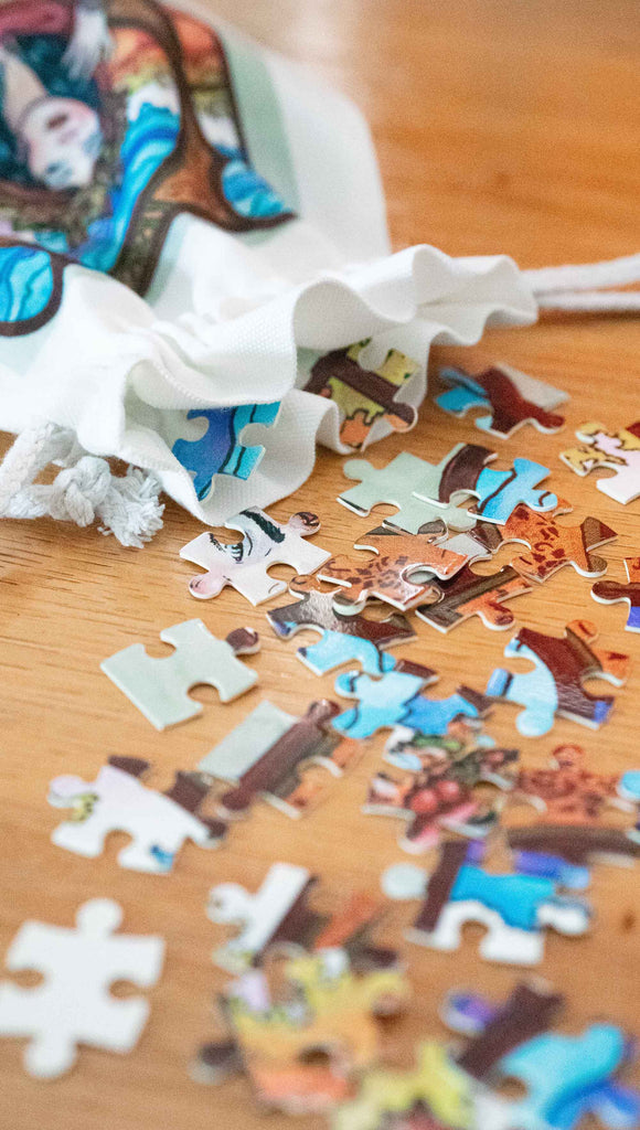 Photo of Art Nouveau Puzzle pieces tumbling from a matching drawcord pouch. Featuring original artwork by Scott Christian Sava. The painting features a woman with a cloak and crown of autumn leaves standing in front of a stained glass window.