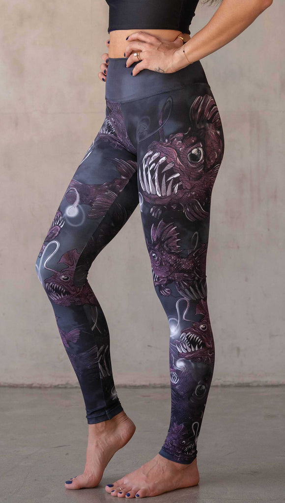 Girl wearing WERKSHOP Angler Fish Athleisure Leggings. The artwork on the leggings feature pink hued/textured angler fish over a black and gray airbrushed background