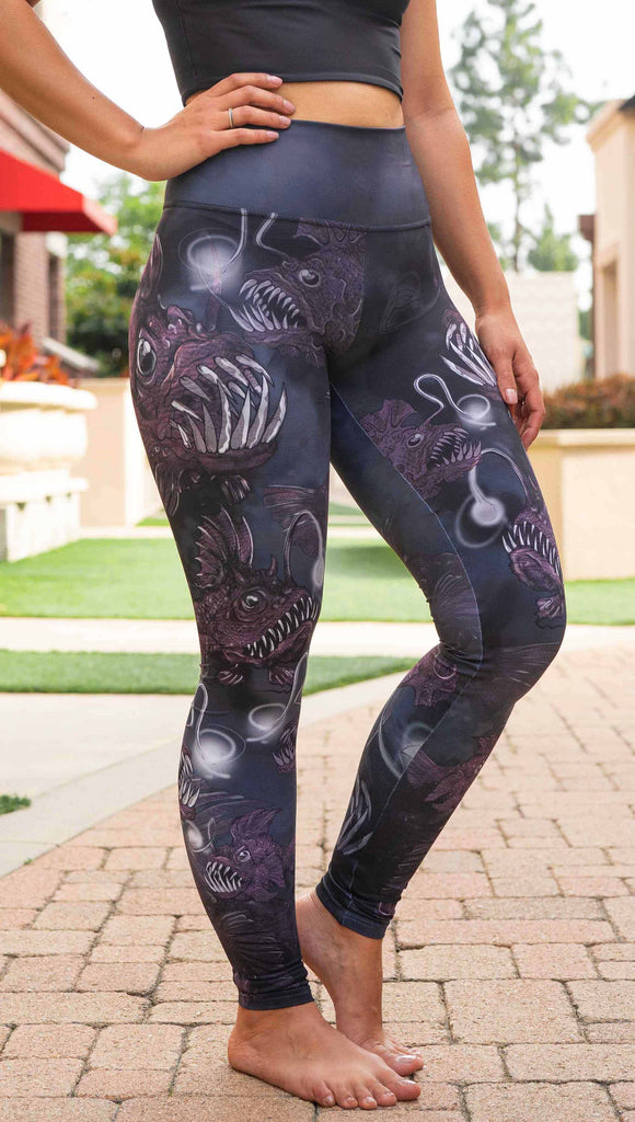 Girl wearing WERKSHOP Angler Fish Athleisure Leggings. The artwork on the leggings feature pink hued/textured angler fish over a black and gray airbrushed background