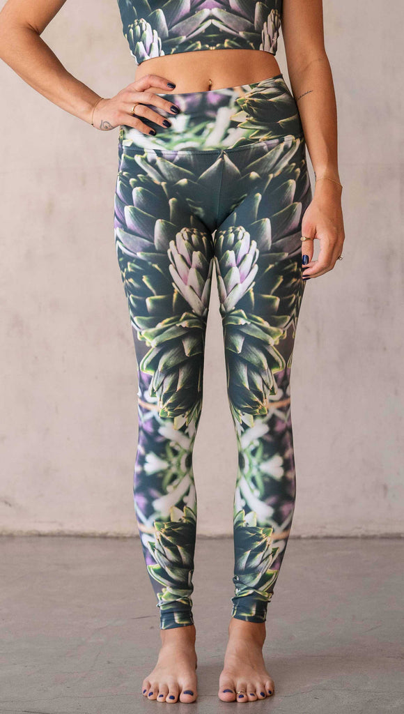 Girl wearing WERKSHOP Artichoke Athleisure Leggings. The leggings show a photo-real fractal inspired edit of artichokes. It has pops of bright green and bright purple over a mostly dark green base. It is a very geometric and fractal design.