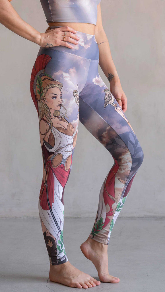 Side view of model wearing WERKSHOP Athena leggings. The leggings are printed with original artwork by Chriztina Marie and features Athena, the goddess of war standing on a cliff’s edge. She is holding a spear with one hand and her owl with the other. She is wearing a greek goddess dress/warrior hat with colors of cream, gold and red. Behind her is a beautiful cloudy sky with rays of light shining down onto her. The model is also wearing a matching top.