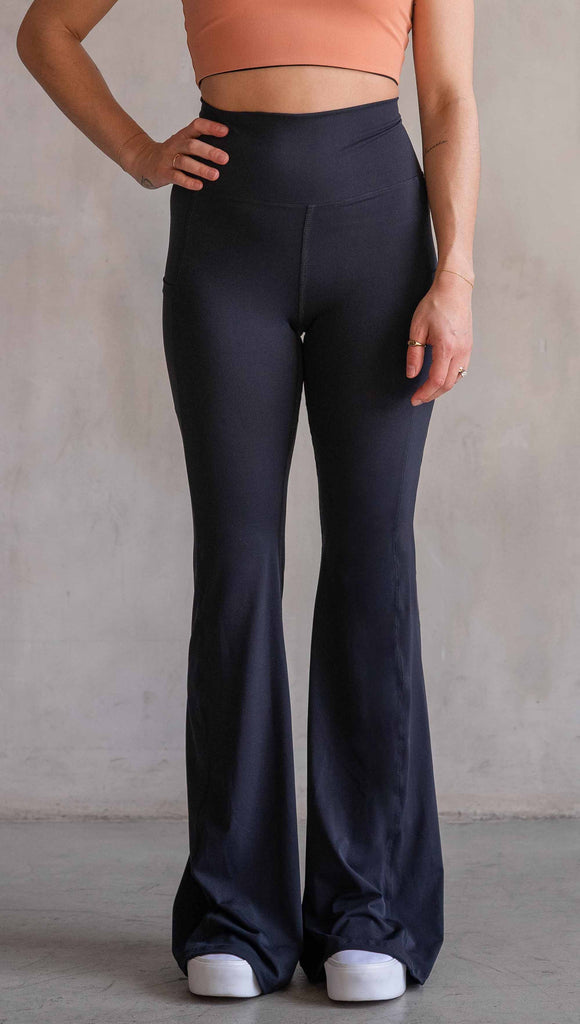 Model wearing WERKSHOP Black EnviSoft Bells. The pants feaure a belled leg opening, flatlock seams, pockets on each thigh, a long panel gusset and small silver eagle logo on the right pocket.