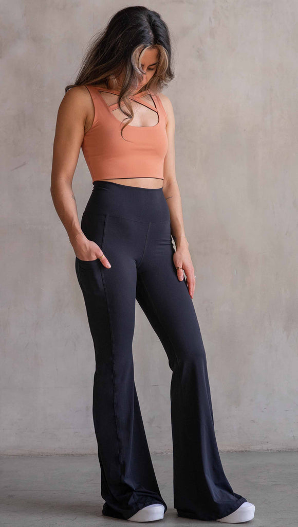 Model wearing WERKSHOP Black EnviSoft Bells. The pants feaure a belled leg opening, flatlock seams, pockets on each thigh, a long panel gusset and small silver eagle logo on the right pocket.