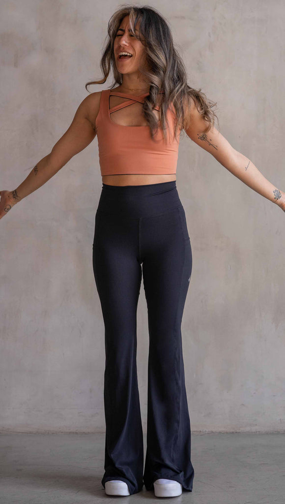 Model wearing WERKSHOP Black EnviSoft Bells. The pants feaure a belled leg opening, flatlock seams, pockets on each thigh, a long panel gusset and small silver eagle logo on the right pocket.