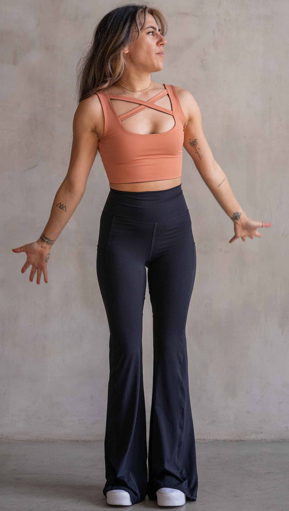 Model wearing WERKSHOP Black EnviSoft Bells. The pants feaure a belled leg opening, flatlock seams, pockets on each thigh, a long panel gusset and small silver eagle logo on the right pocket.