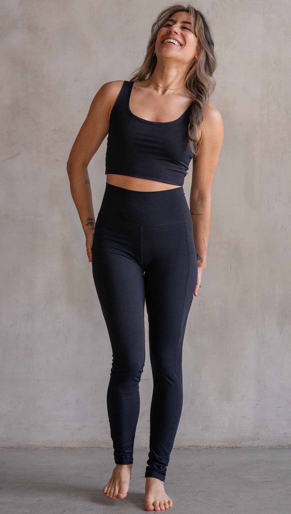 Model wearing WERKSHOP Solid Black EnviSoft Leggings. Featuring pockets on each thigh, a long panel gusset, flatlock seams and an eagle logo on the right pocket.