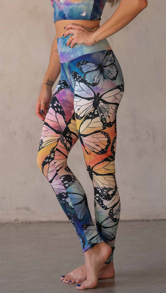 Girl wearing WERKSHOP Butterflies Athleisure Leggings. The artwork on the leggings features a black outline of monarch butterflies over a rainbow coloured watercolor background.