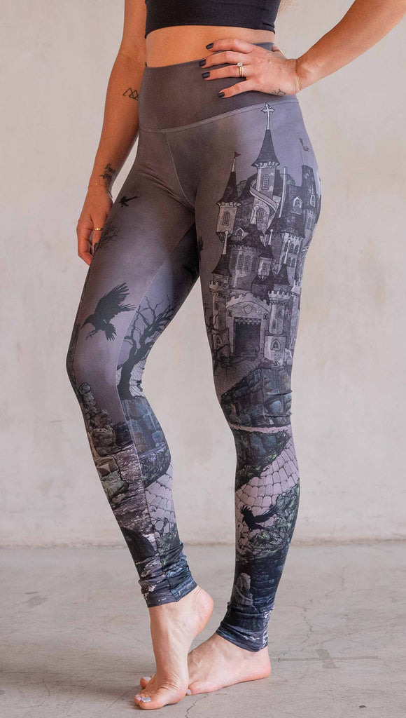 Model wearing WERKSHOP Dark Castle Leggings. The artwork on the leggings feature a fully monochrome (black and gray) gothic castle with stone walkway and crows flying in the moonlight.