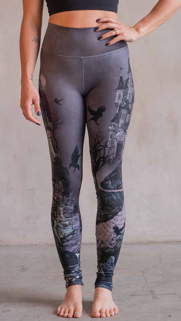 Model wearing WERKSHOP Dark Castle Leggings. The artwork on the leggings feature a fully monochrome (black and gray) gothic castle with stone walkway and crows flying in the moonlight.