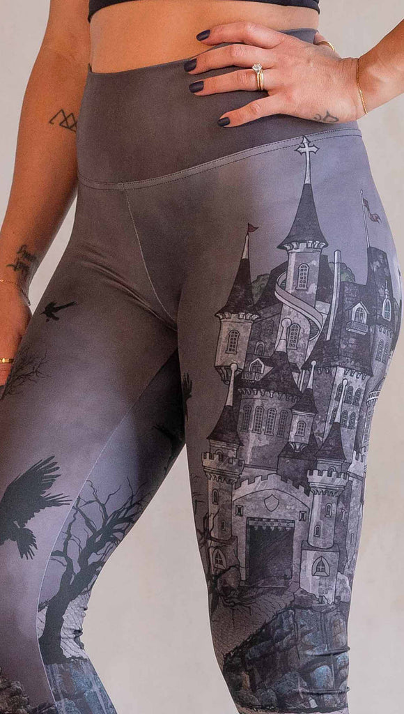 Model wearing WERKSHOP Dark Castle Leggings. The artwork on the leggings feature a fully monochrome (black and gray) gothic castle with stone walkway and crows flying in the moonlight.