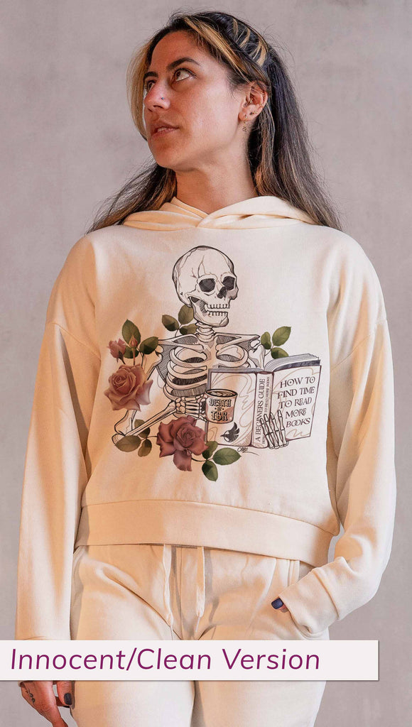 Model wearing WERKSHOP  "Death by TBR" Hoodie in Bone Colorway ~ Innocent/Clean version with the phrase, "How to Find Time to Read More Books". Featuring a skeleton holding a book in one hand and a coffee mug in the other with accent roses.