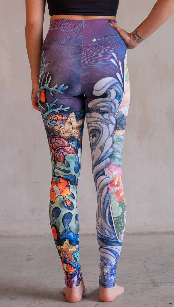 Model wearing WERKSHOP Clownfish and Surf Mashup Leggings. These leggings feature two iconic prints. on the right leg, you have a surfboard with dolphins and spashing waves. On the left leg, you have an explosion of color with a coral reef and clownfish.