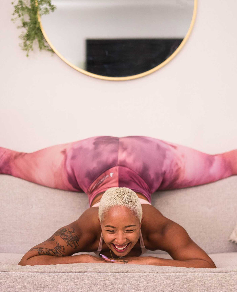 Girl laughing on a couch while doing the splits and wearing WERKSHOP rose quart athleisure leggings and vanilla sports bra