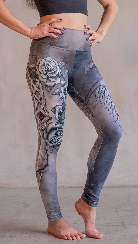 Model wearing WERKSHOP Dagger Mashup Leggings. One leg has a dagger with a wreath of roses. The other leg has an abstract gargoyle-esc dragon. Both legs are neutral in color tone with the right leg being a bit taupe and the left leg being a cool gray.