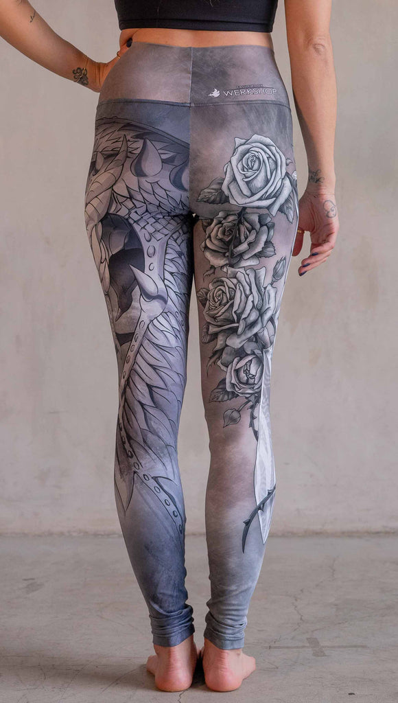 Model wearing WERKSHOP Dagger Mashup Leggings. One leg has a dagger with a wreath of roses. The other leg has an abstract gargoyle-esc dragon. Both legs are neutral in color tone with the right leg being a bit taupe and the left leg being a cool gray.