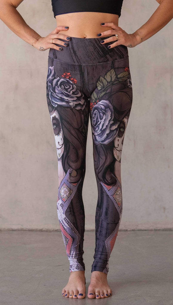 Girl wearing WERKSHOP "Dark Sugar" Athleisure leggings. The artwork on the leggings features a girl wearing dia de los muertos makeup in tones of blue and gray. she is wearing a crown of roses and a beaded necklace over a distressed warm gray woodgrain background.