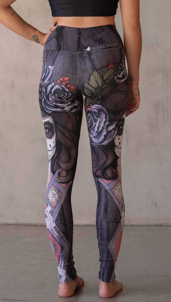 Girl wearing WERKSHOP "Dark Sugar" Athleisure leggings. The artwork on the leggings features a girl wearing dia de los muertos makeup in tones of blue and gray. she is wearing a crown of roses and a beaded necklace over a distressed warm gray woodgrain background.