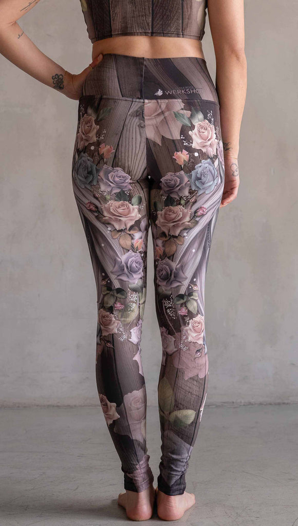 Model wearing WERKSHOP Dark Unicorn Athleisure Leggings. The leggings feature original artwork of a unicorn surrounded by a wreath of vintage coloured roses. The unicorn has a beaded chain with a skull dangling from it's horn. The artwork is over a warm woodgrain background.