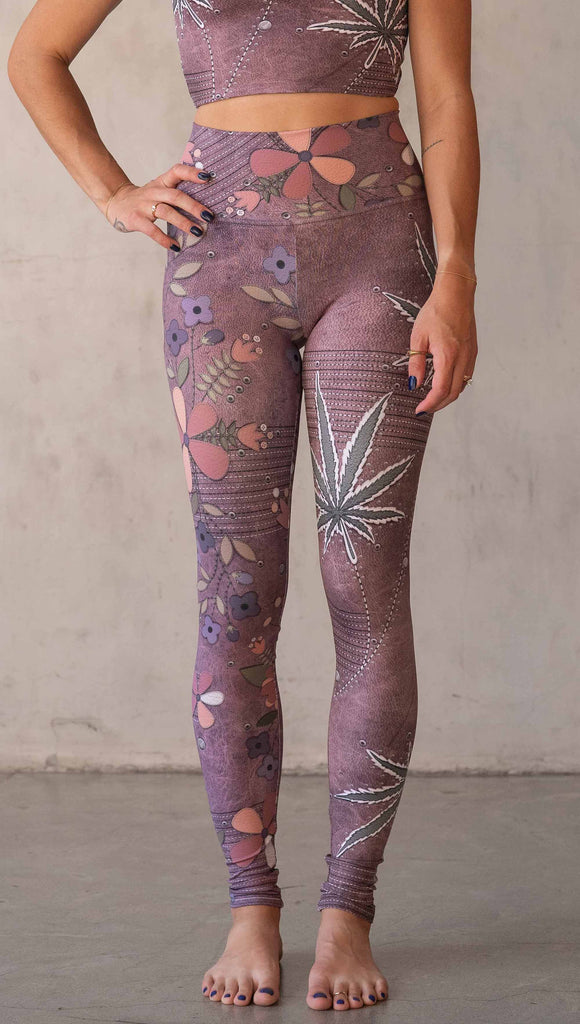 Model wearing WERKSHOP Dope + Flowers Mashup leggings. The leggings are printed with original artwork by Chriztina Marie. One leg features patchwork daisys over grainy mauve toned leather background. The other leg features marijuana leaves over a warm brown background. Both legs have faux stitching.