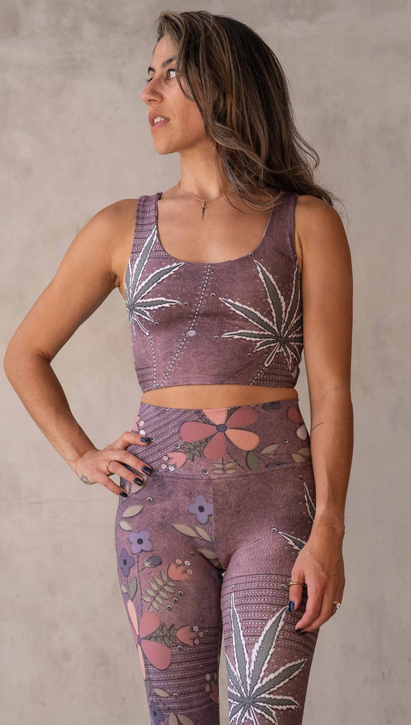 Model wearing WERKSHOP Dope + Flowers Reversible top. One side of the top features patchwork daisys over grainy mauve toned leather background. The opposite side of the top features marijuana leaves over a warm brown background. Both legs have faux stitching and a small eagle logo on the bottom left sweep.