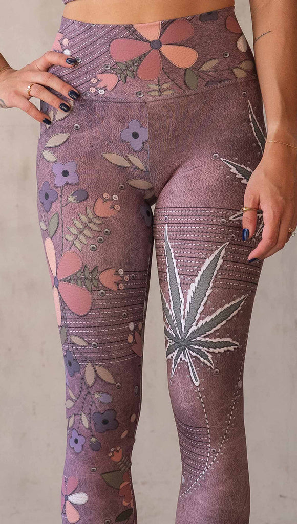 Model wearing WERKSHOP Dope + Flowers Mashup leggings. The leggings are printed with original artwork by Chriztina Marie. One leg features patchwork daisys over grainy mauve toned leather background. The other leg features marijuana leaves over a warm brown background. Both legs have faux stitching.