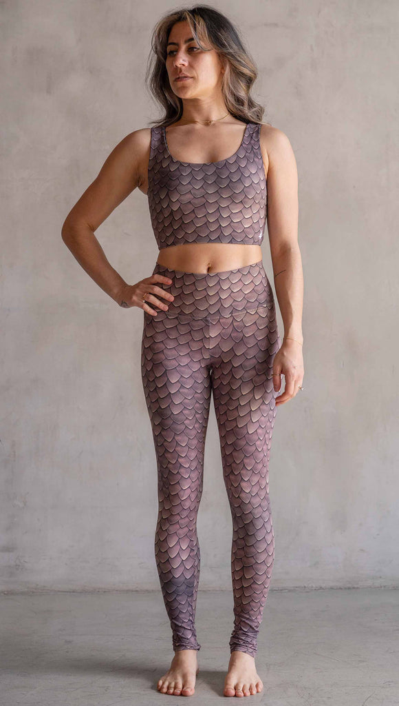 Model wearing WERKSHOP Dragon Scales leggings. The artwork on the leggings features small pointed scales in a warm taupe/gold color pallet.