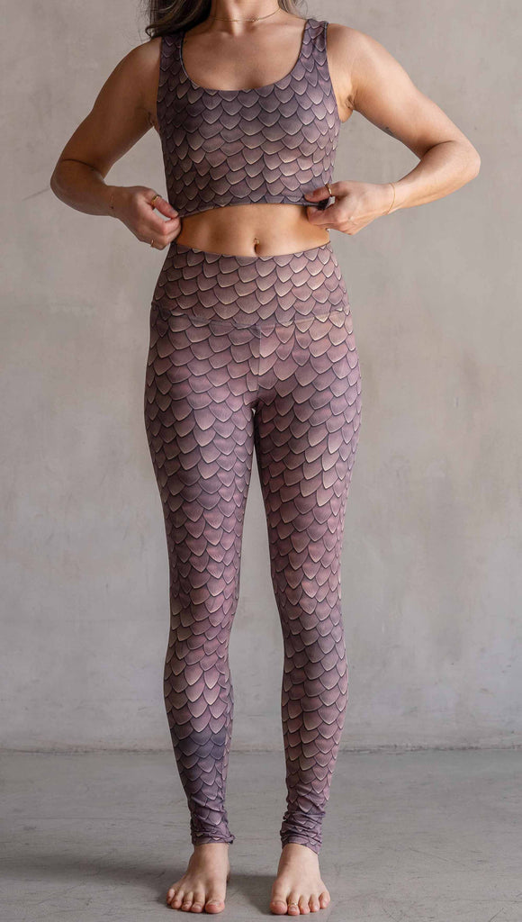 Model wearing WERKSHOP Dragon Scales leggings. The artwork on the leggings features small pointed scales in a warm taupe/gold color pallet.