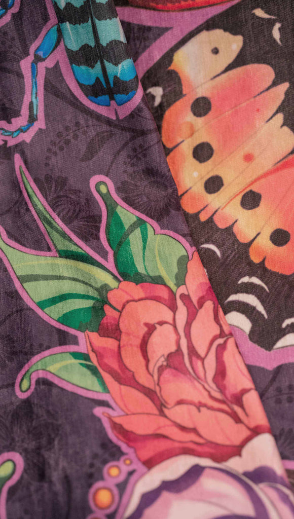 WERKSHOP Enchanted Garden tapestry draped on a couch. The tapestry is printed with original artwork by Chriztina Marie. The artwork printed not the fabric features Butterflies, Beetles and Peonies over a warm fuchsia with bright bold pops of color on each beetle and Butterfly.