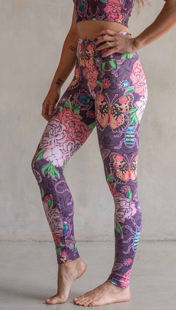 Side view of model wearing WERKSHOP Enchanted Garden Athleisure Leggings. The fabric is printed with original artwork by our Female Founder, Chriztina Marie. The artwork printed not the fabric features Butterflies, Beetles and Peonies over a warm fuchsia with bright bold pops of color on each beetle and Butterfly.