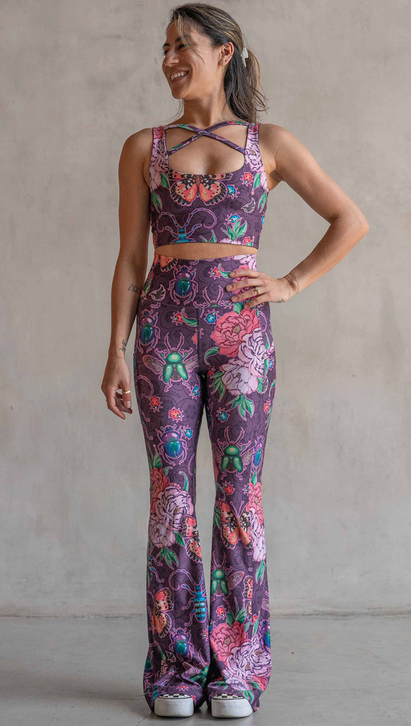 Full body front view of model wearing WERKSHOP Enchanted Garden EnviSoft Bell Bottom pants with Pockets. The fabric is printed with original artwork by our Female Founder, Chriztina Marie. The artwork printed not the fabric features Butterflies, Beetles and Peonies over a warm fuchsia with bright bold pops of color on each beetle and Butterfly.