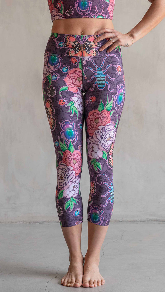 Front view of model wearing WERKSHOP Enchanted Garden Capri Length Triathlon Leggings. The fabric is printed with original artwork by our Female Founder, Chriztina Marie. The artwork printed not the fabric features Butterflies, Beetles and Peonies over a warm fuchsia with bright bold pops of color on each beetle and Butterfly.