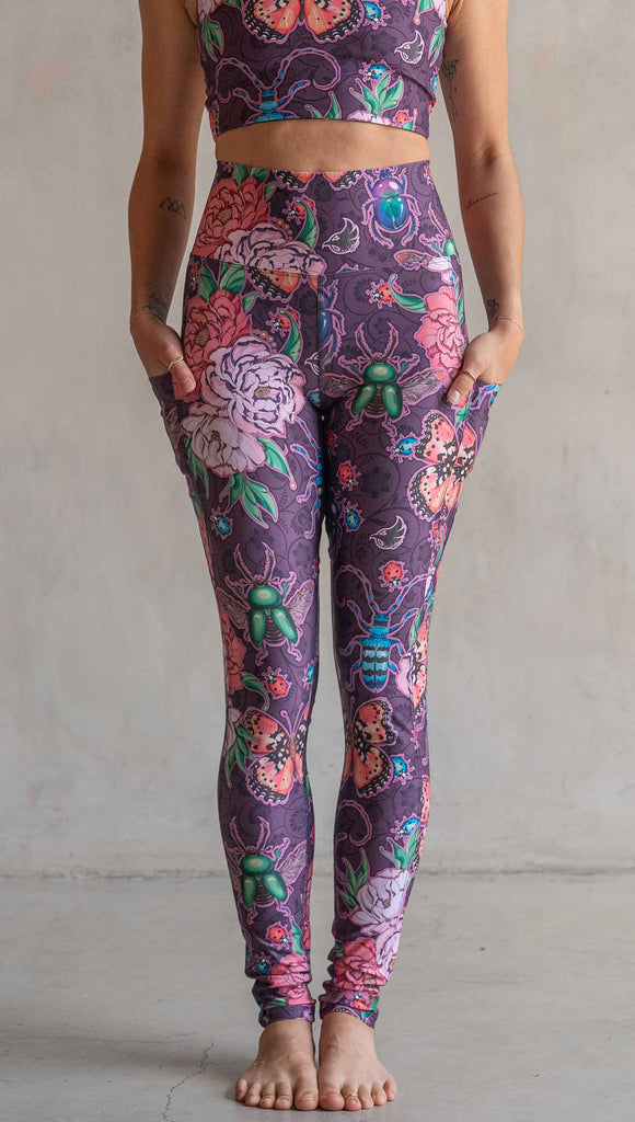 Front view of model wearing WERKSHOP Enchanted Garden EnviSoft Leggings with Pockets. The fabric is printed with original artwork by our Female Founder, Chriztina Marie. The artwork printed not the fabric features Butterflies, Beetles and Peonies over a warm fuchsia with bright bold pops of color on each beetle and Butterfly.