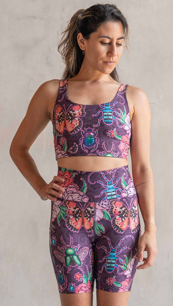 Front view of model wearing WERKSHOP Enchanted Garden EnviSoft Bicycle length shorts with pockets. The fabric is printed with original artwork by our Female Founder, Chriztina Marie. The artwork printed not the fabric features Butterflies, Beetles and Peonies over a warm fuchsia with bright bold pops of color on each beetle and Butterfly.