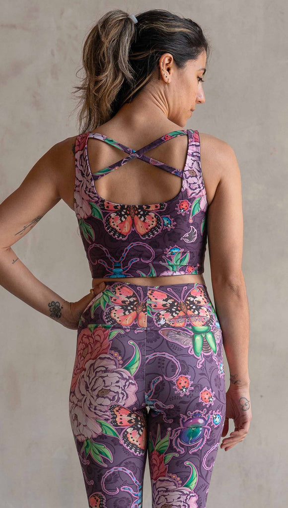 Back view of model wearing WERKSHOP Starlings and Enchanted Garden 4-Way reversible top. The fabric is printed with original artwork by Chriztina Marie. One side features European Starlings perched on a branch near a crescent moon and fireflies. The colors are warm purples with pops of pink, gold and green. The other side features Butterflies, Beetles and Peonies over a warm fuchsia with bright bold pops of color on each beetle and Butterly.