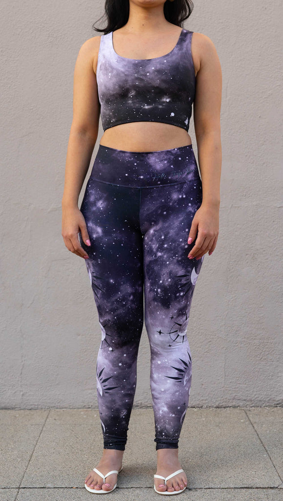 Model wearing "Feyre's Tattoo" Leggings with a dark purplish-blue to black ombre celestial background and moon phases on each leg. Officially licensed for A Court of Thorns and Roses by Sarah J Maas. It has the phrase, "Hello, Feyre Darling" on the waistband.