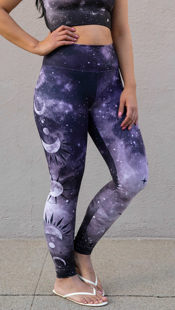 Model wearing "Feyre's Tattoo" Leggings with a dark purplish-blue to black ombre celestial background and moon phases on each leg. Officially licensed for A Court of Thorns and Roses by Sarah J Maas. It has the phrase, "Hello, Feyre Darling" on the waistband.