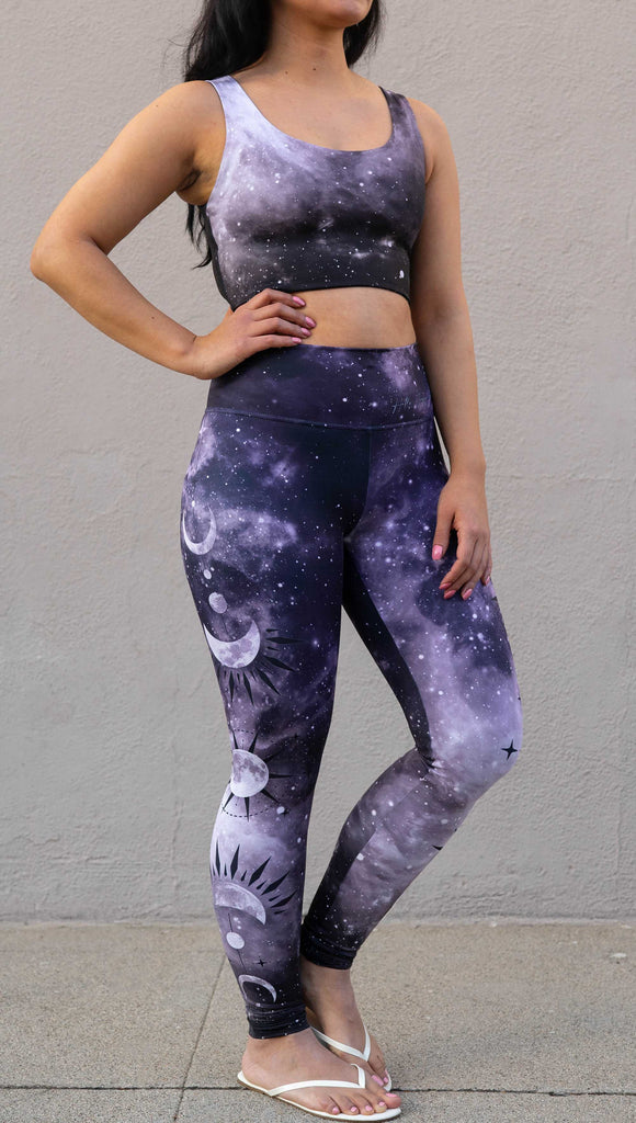 Model wearing "Feyre's Tattoo" Leggings with a dark purplish-blue to black ombre celestial background and moon phases on each leg. Officially licensed for A Court of Thorns and Roses by Sarah J Maas. It has the phrase, "Hello, Feyre Darling" on the waistband.