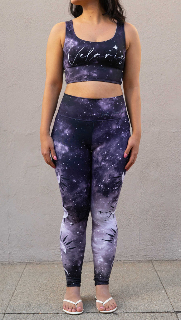 Model wearing "Feyre's Tattoo" Leggings with a dark purplish-blue to black ombre celestial background and moon phases on each leg. Officially licensed for A Court of Thorns and Roses by Sarah J Maas. It has the phrase, "Hello, Feyre Darling" on the waistband.