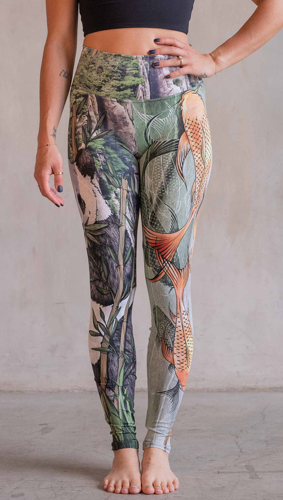  Model wearing WERKSHOP Koi Fish and Giant Panda Mashup Leggings. The wearer's right leg has an illustration of a panda eating bamboo with a gorgeous background of mountains. The wearers right leg has koi fishies swimming over an abstract taupe and forest green background.