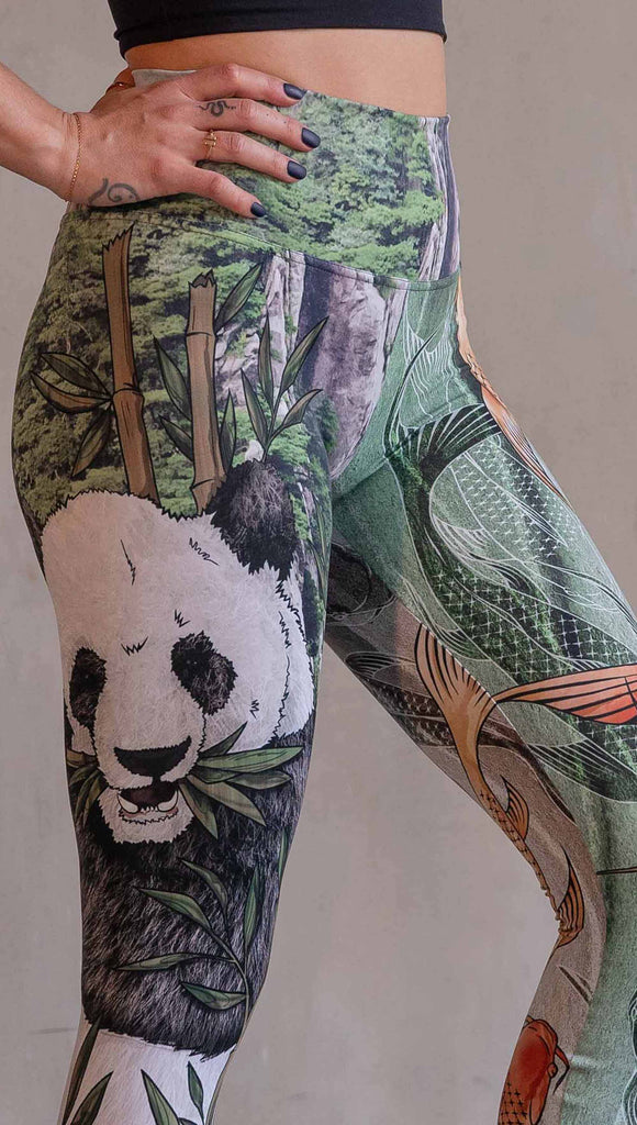  Model wearing WERKSHOP Koi Fish and Giant Panda Mashup Leggings. The wearer's right leg has an illustration of a panda eating bamboo with a gorgeous background of mountains. The wearers right leg has koi fishies swimming over an abstract taupe and forest green background.