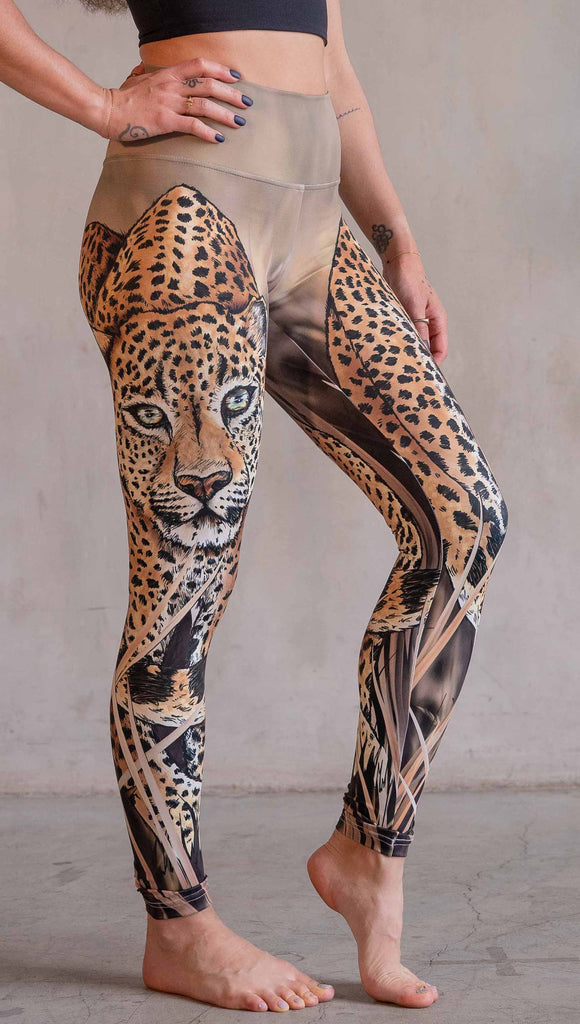 Model wearing WERKSHOP Leopard Leggings. The leggings feature original and exclusive artwork of a Leopard walking through the brush. The leggings are all khaki and tan tones with little pops of green in the leopards eyes.