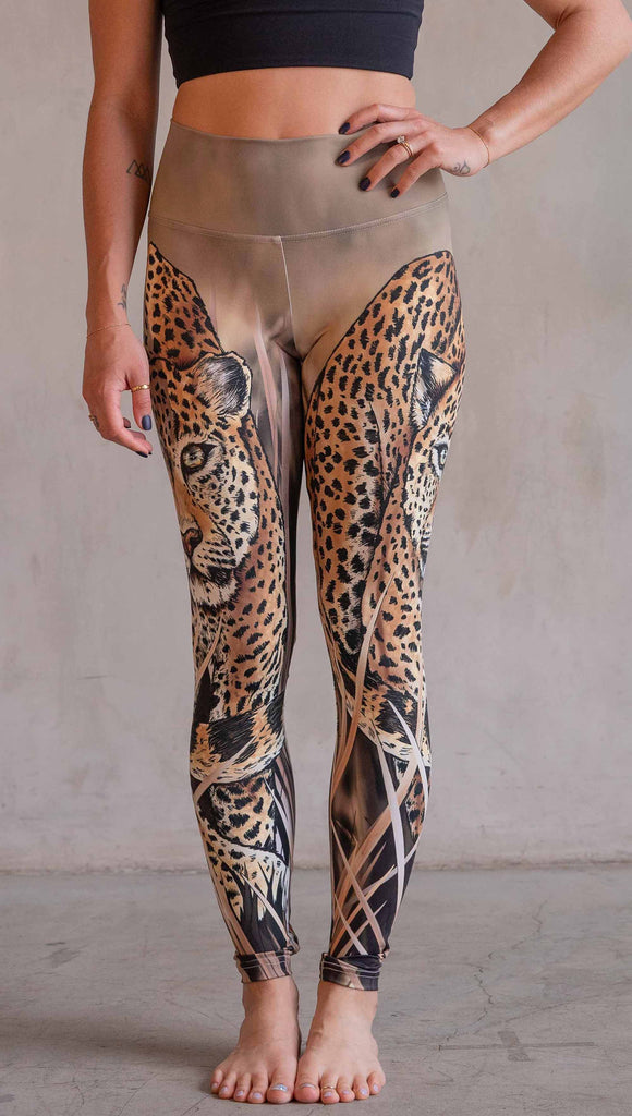 Model wearing WERKSHOP Leopard Leggings. The leggings feature original and exclusive artwork of a Leopard walking through the brush. The leggings are all khaki and tan tones with little pops of green in the leopards eyes.