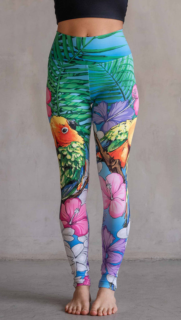 Model wearing WERKSHOP Lovebirds Athleisure Leggings. The leggings feature original and exclusive artwork by Chriztina Marie of two lovebirds snuggling and surrounded by hibiscus flowers. The overall design is very tropical and asymmetrical.