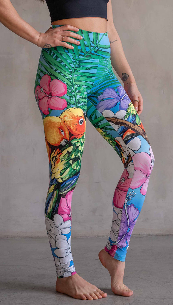 Model wearing WERKSHOP Lovebirds Athleisure Leggings. The leggings feature original and exclusive artwork by Chriztina Marie of two lovebirds snuggling and surrounded by hibiscus flowers. The overall design is very tropical and asymmetrical.