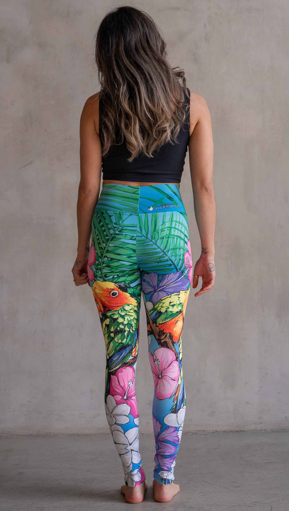 Model wearing WERKSHOP Lovebirds Athleisure Leggings. The leggings feature original and exclusive artwork by Chriztina Marie of two lovebirds snuggling and surrounded by hibiscus flowers. The overall design is very tropical and asymmetrical.