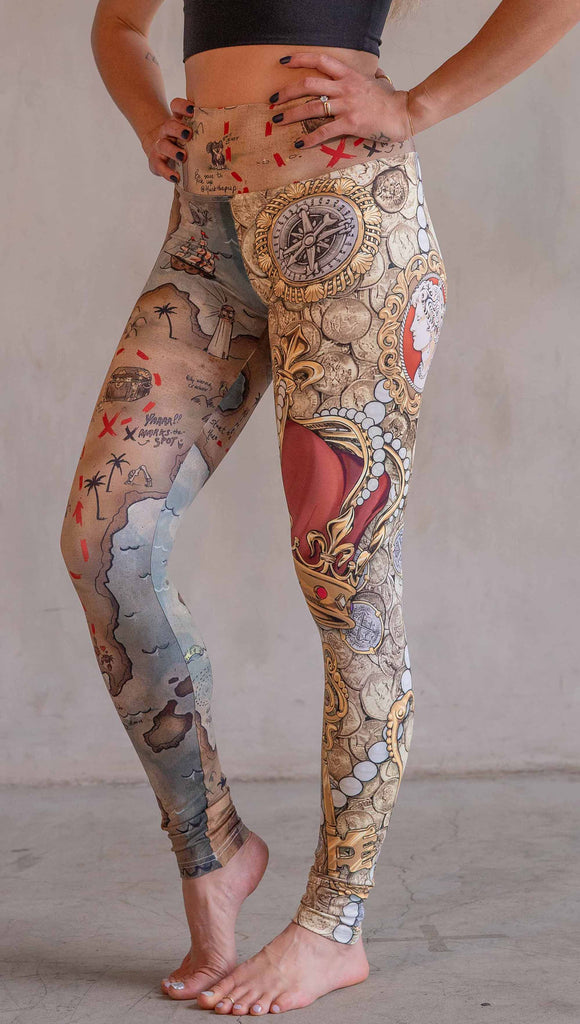 Model wearing WERKSHOP Booty Mashup Leggings. The wearer's right leg is printed with vintage inspired, hand drawn, treasure map artwork and the left leg is golden treasure with a kings royal crown, keys and pearls: everything you'd expect to find inside a pirates treasure.